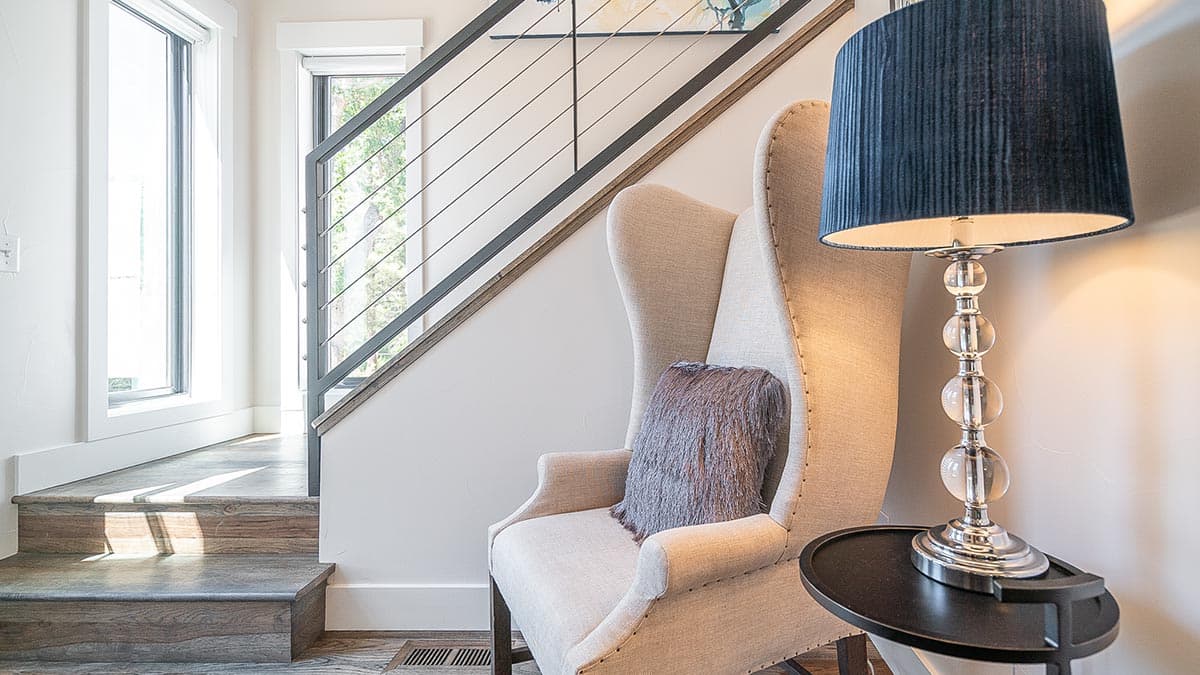 Interior view of a staircase with modern cable railings, a wingback chair, and a tall lamp.