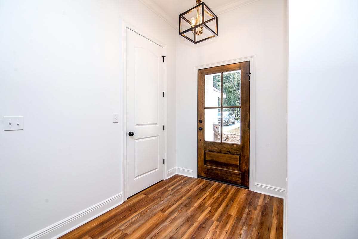 Interior view: Entryway with white paneled door, wooden glass door, and wood-look flooring. Geometric lantern light fixture overhead.
