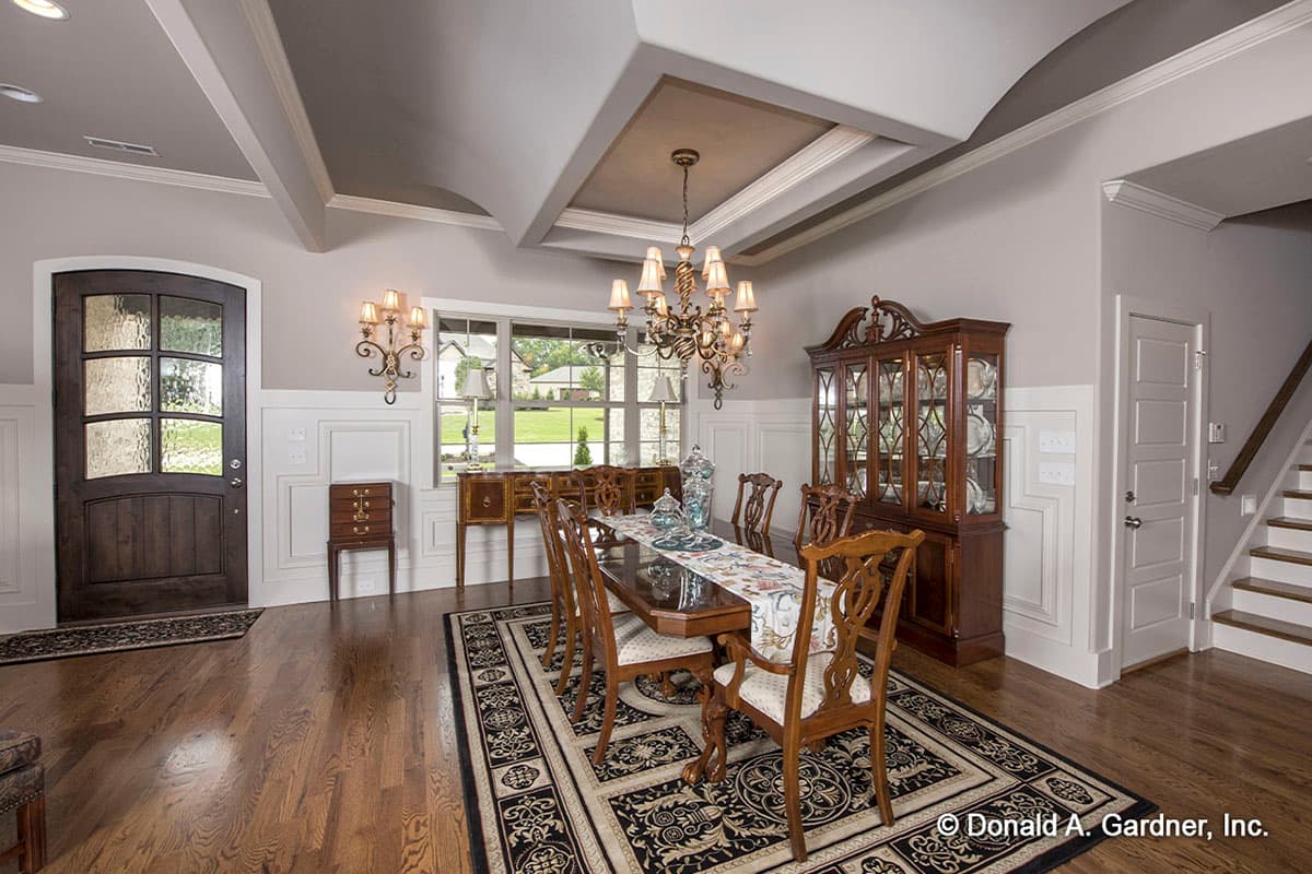 Formal dining room with coffered ceiling, chandelier, wainscoting, dark wood door, and formal dining set.