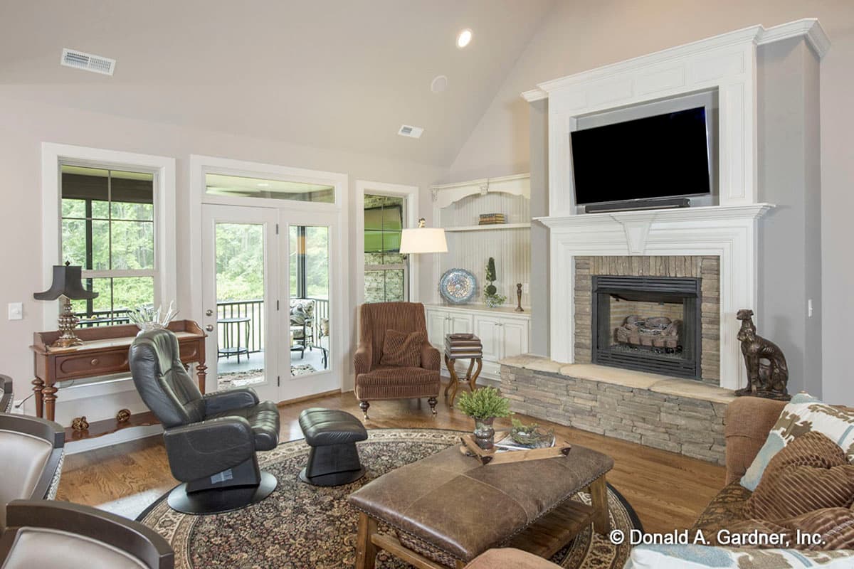 Living room with vaulted ceiling, stone fireplace with mounted TV, built-in shelving, and french doors opening to a covered porch.