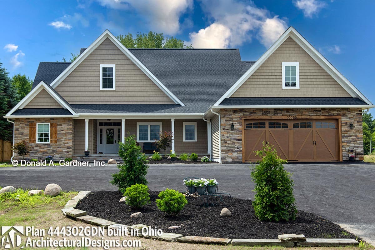 House plan exterior: Two-story home with stone foundation, covered porch, dual gables, and a side-facing garage with wood doors.