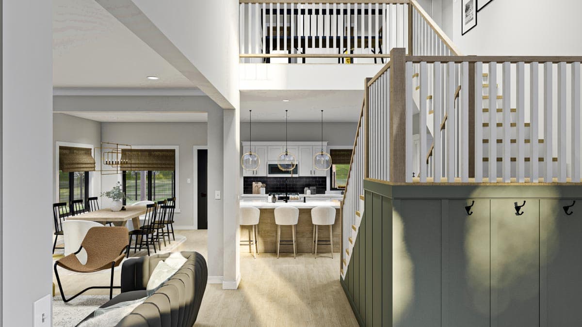 Interior view of a house showing a dining area, kitchen with island and bar stools, and a staircase with white balusters and wood accents.