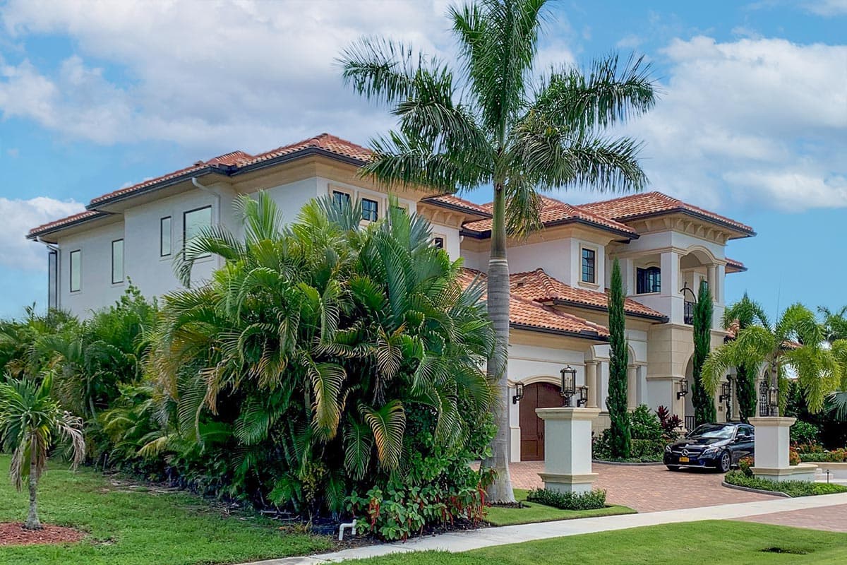 House plan exterior featuring two-story structure, tile roof, columns, and a covered entry. Includes a three-car garage and manicured landscaping.