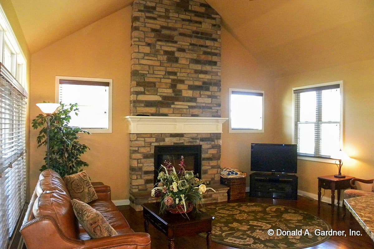 Living room interior with vaulted ceiling, stone fireplace, leather sofa, and large windows.