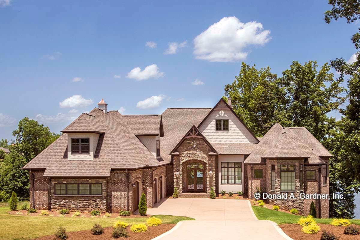 House plan exterior: Two-story home with brick and stone accents, prominent gables, dormers, and a central arched entryway.