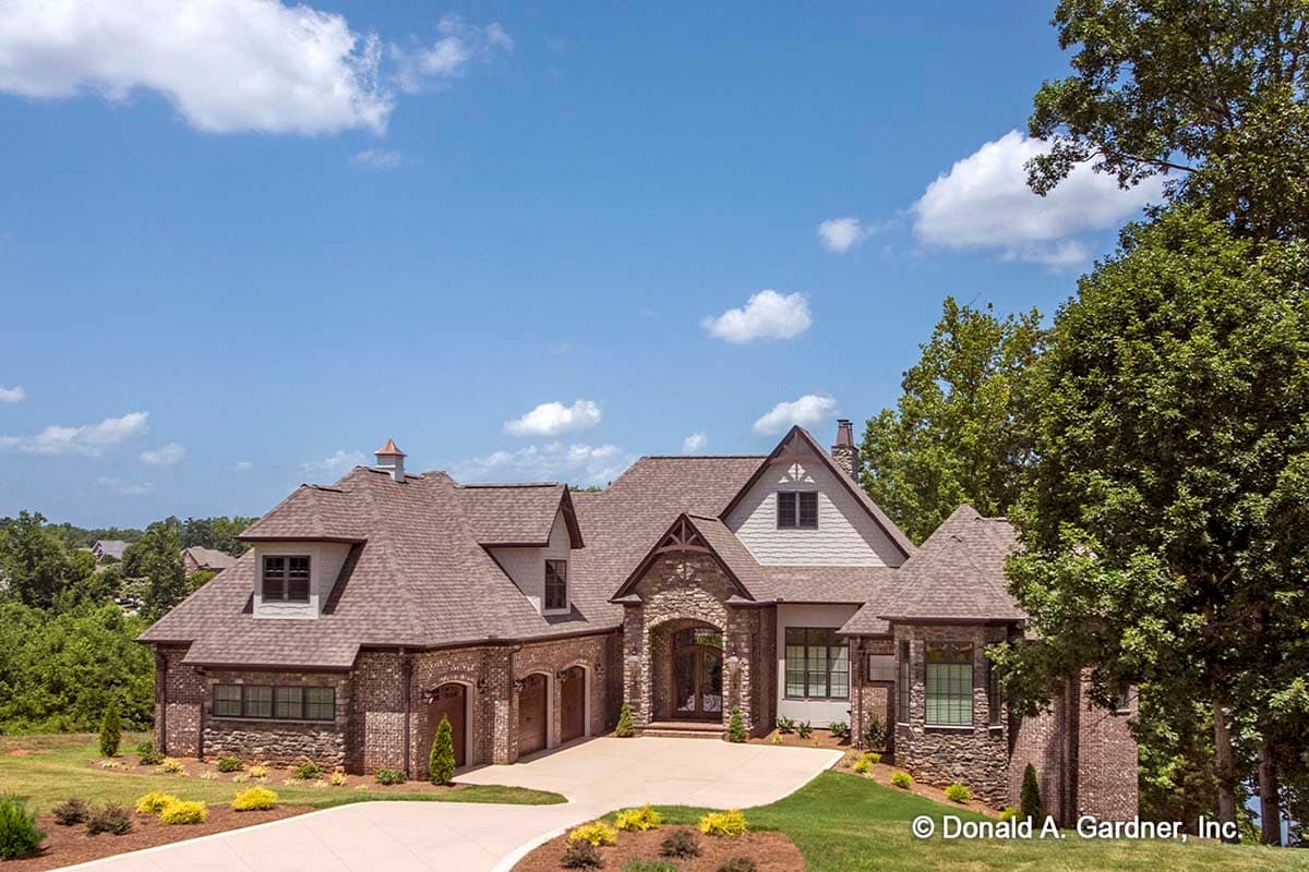 House plan exterior showing a multi-story residence with stone and brick facade, arched entryway, and multiple gables.