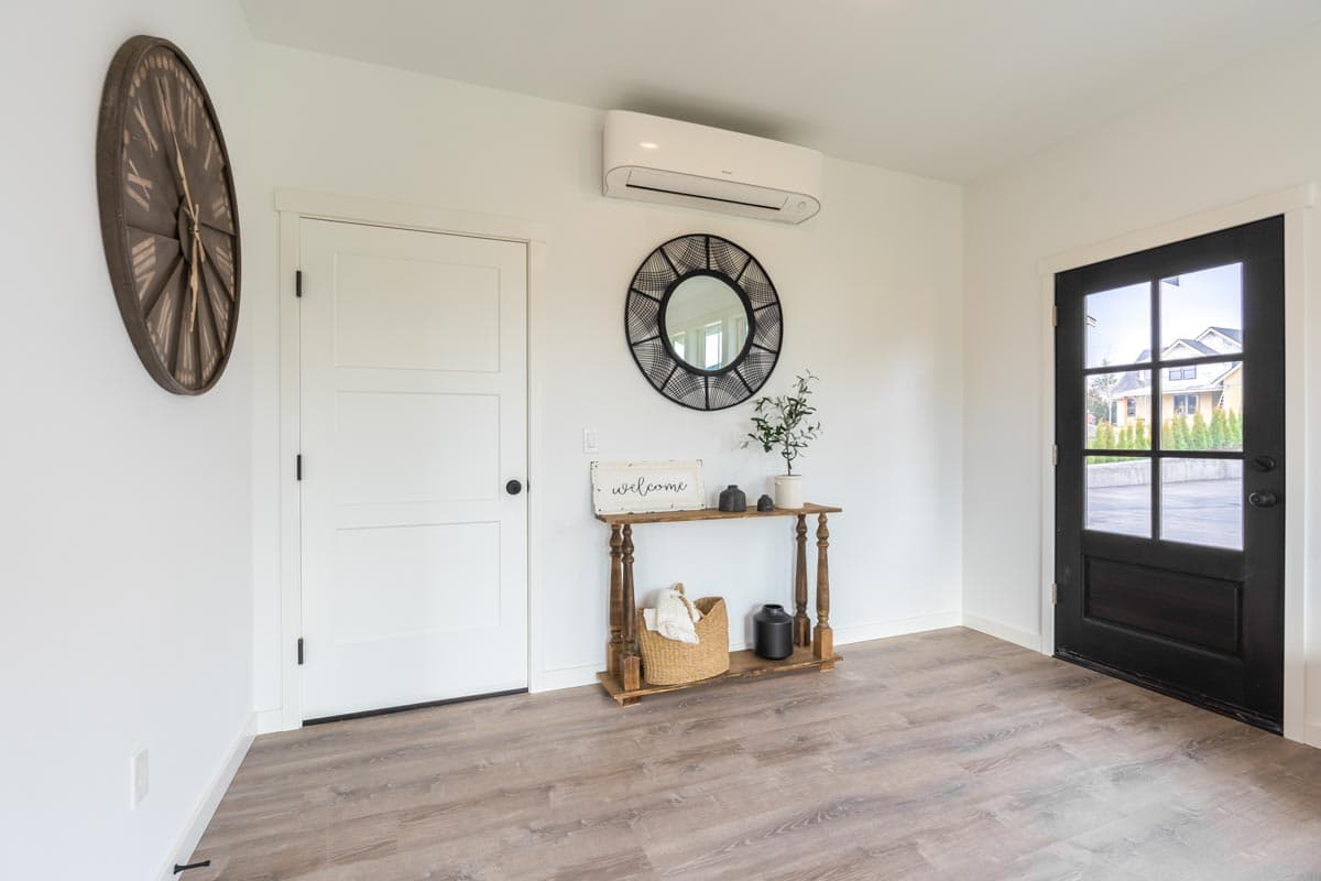 Interior entryway with white panel door, black glass door, console table, mirror, and air conditioning unit.