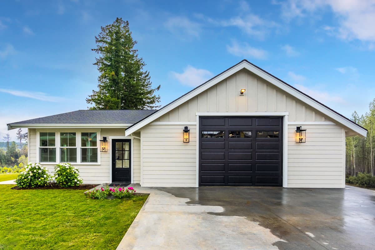 House plan exterior featuring a single-story design, a gable roof, and an attached garage with dark door. Includes a front entry door.