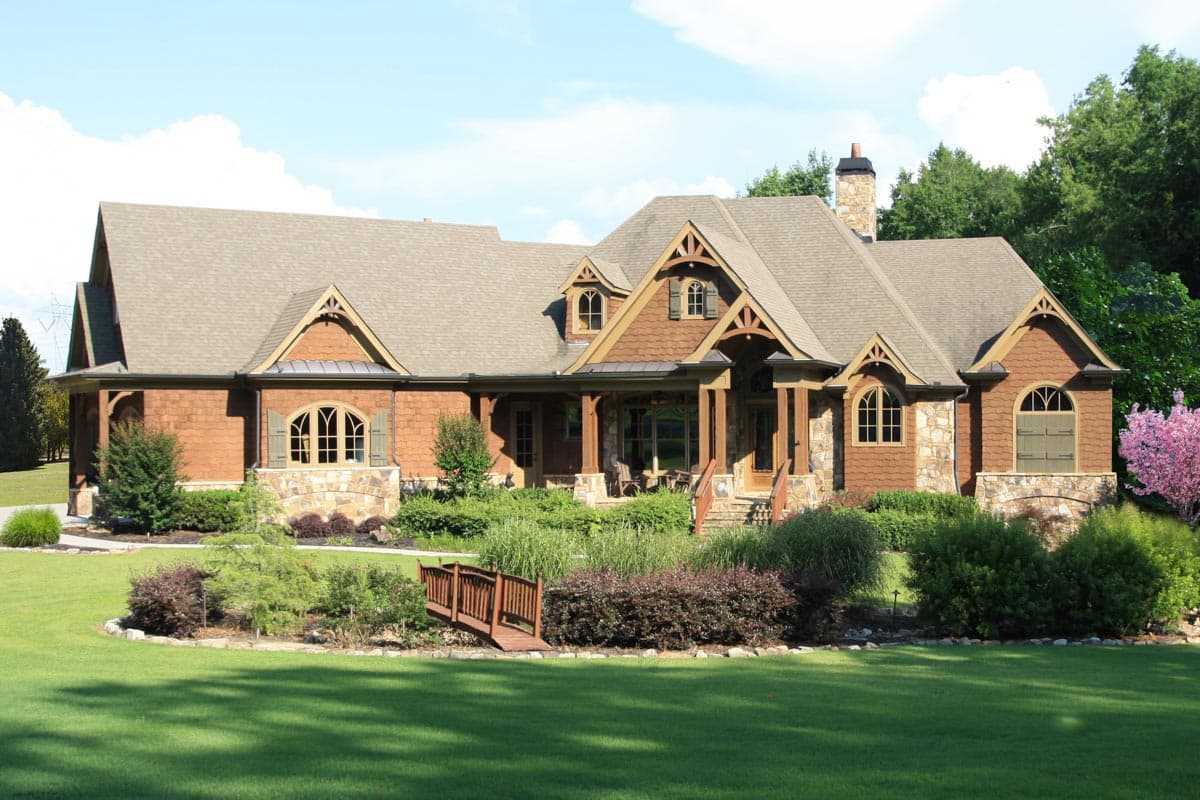 House plan exterior. Craftsman style, one-story. Features include gables, dormers, a covered porch, and a stone chimney.