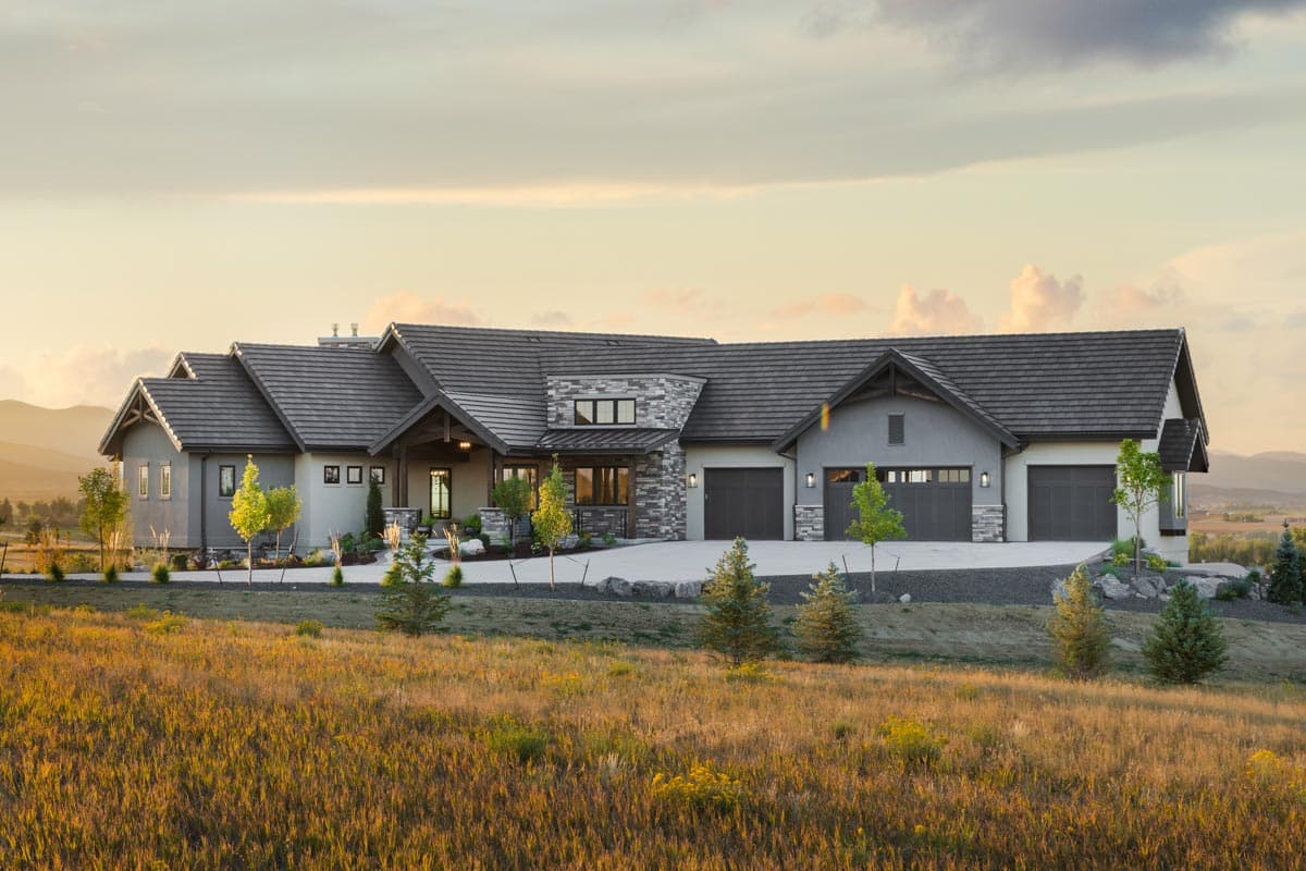 House plan exterior. One-story Ranch-style home with multiple gabled roof sections, stone accents, and an attached three-car garage.