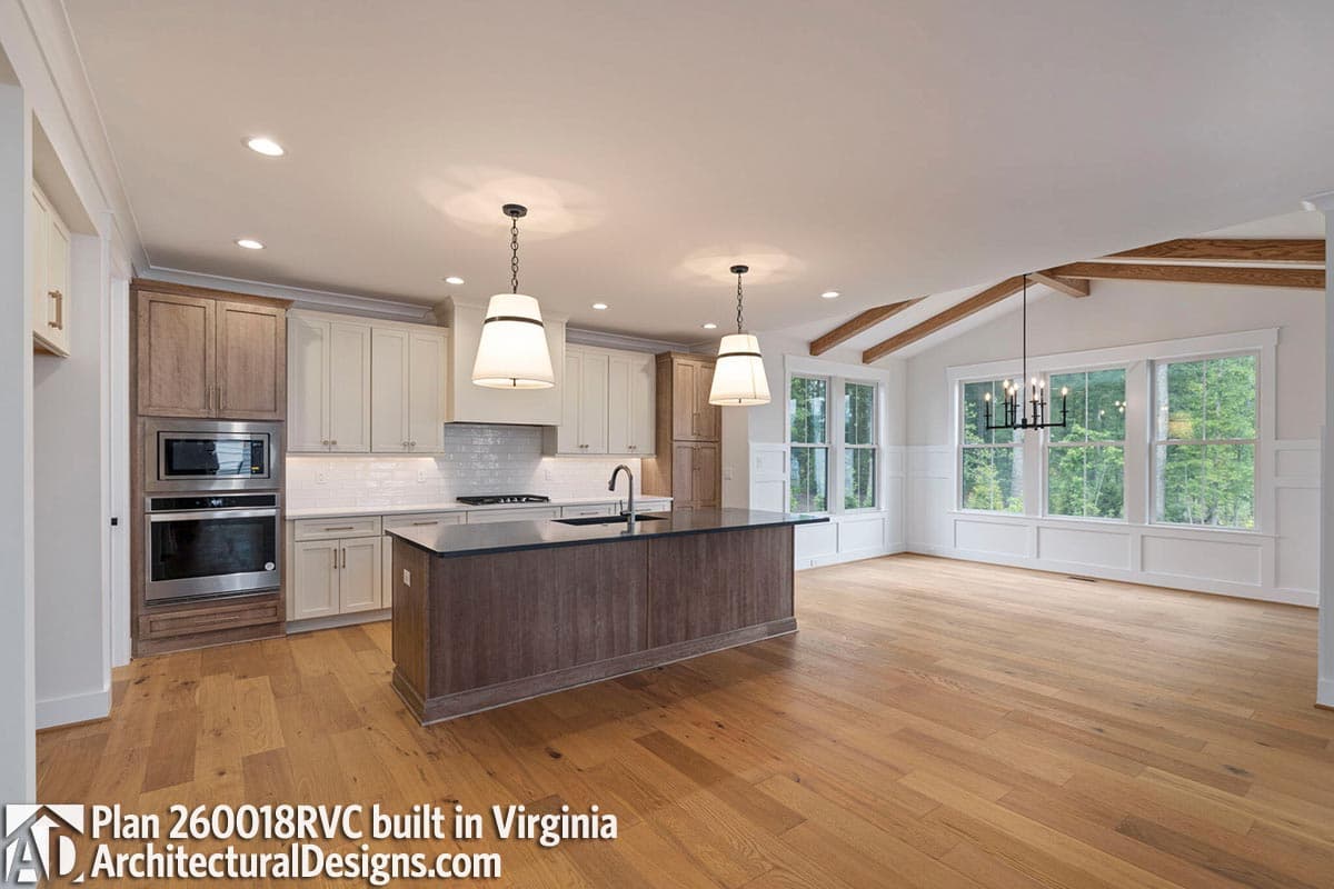 Open-concept kitchen and great room with vaulted ceiling, exposed beams, island, and large windows.