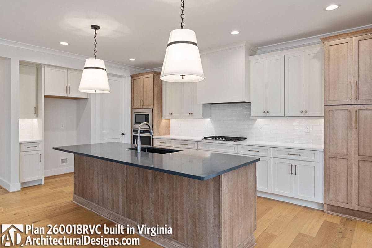 Kitchen interior with large island, white subway tile backsplash, stainless steel appliances, and light wood floors.