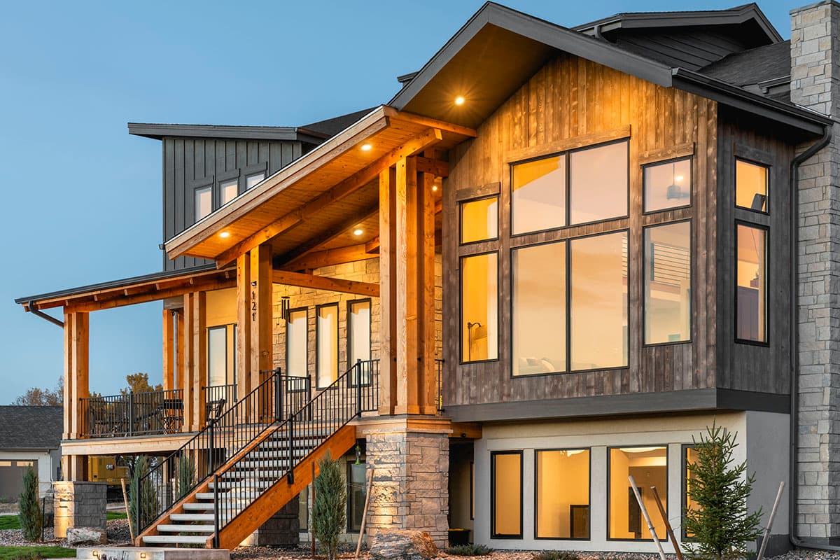 House plan exterior: Modern style, wood siding, stone accents, large windows, covered porch with wood beams, and elevated staircase.
