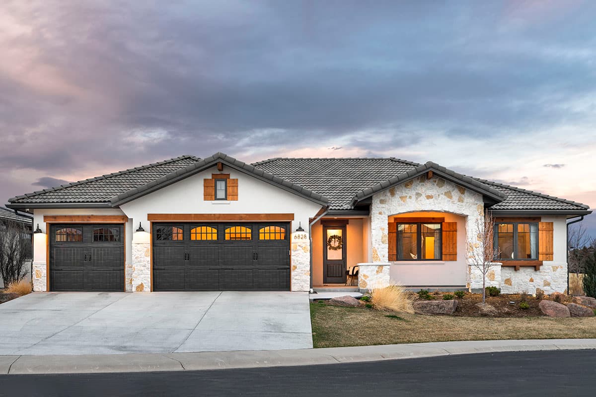 House plan exterior featuring a single-story design, stone accents, gabled roof, and two garage bays with dark doors.