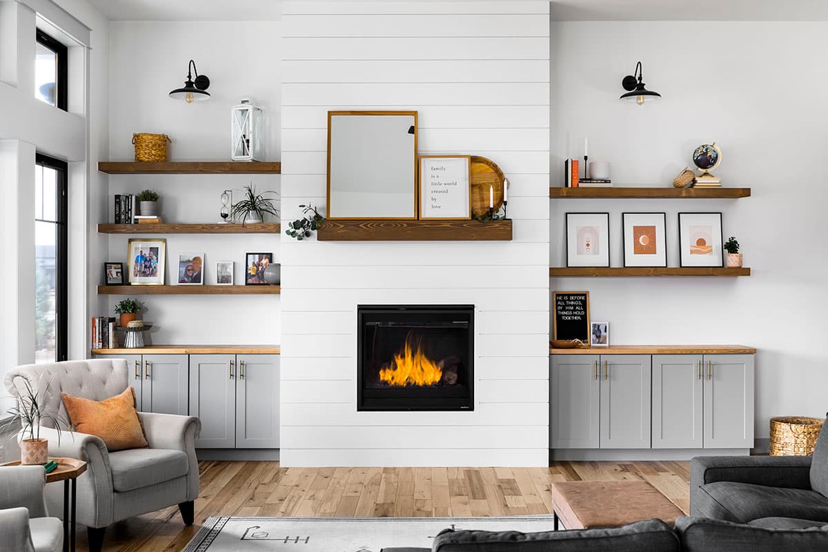 Living room with fireplace, shiplap wall, floating shelves with decor, and built-in cabinetry.
