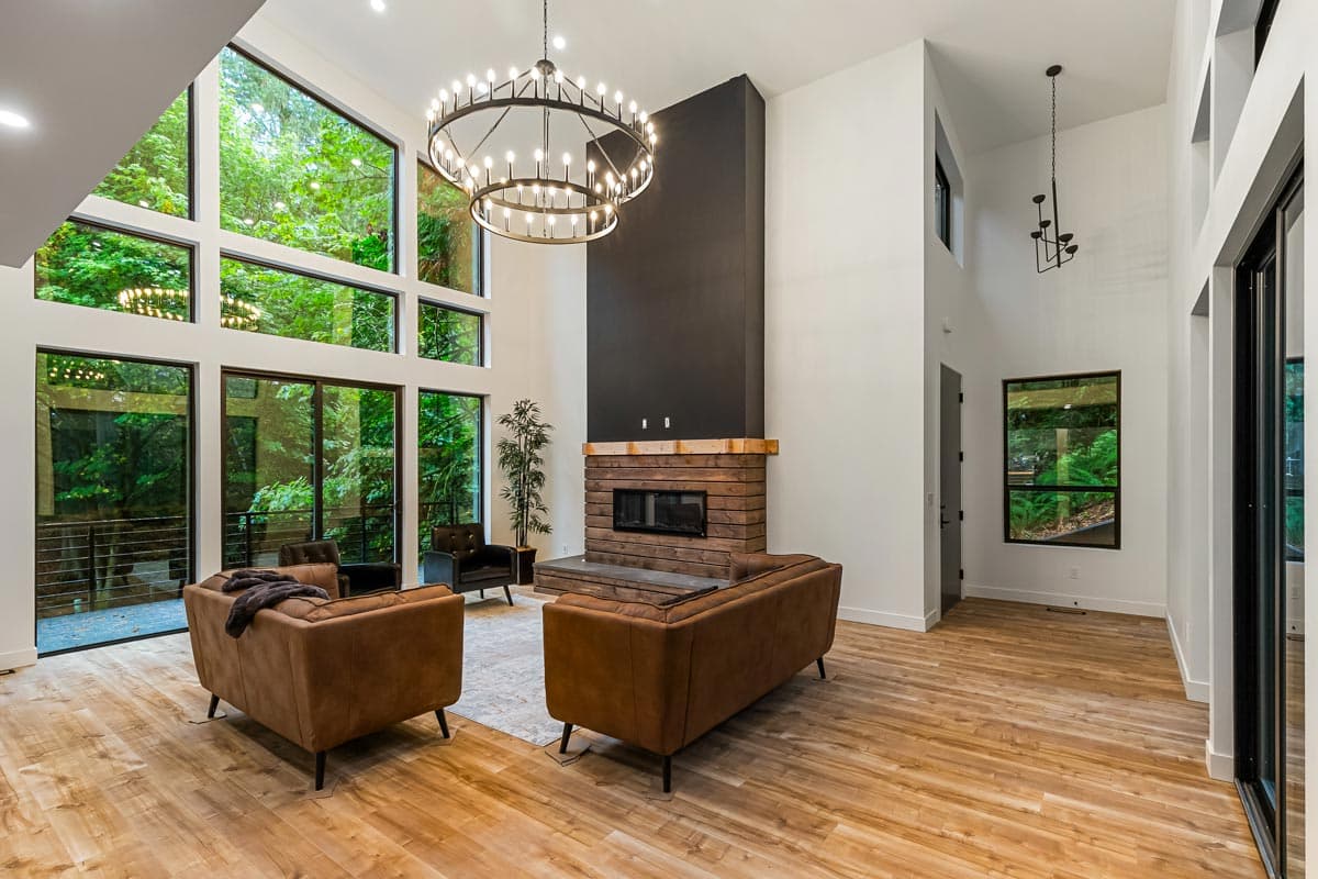 Great room with vaulted ceiling, floor-to-ceiling windows, brick fireplace, and modern chandelier.