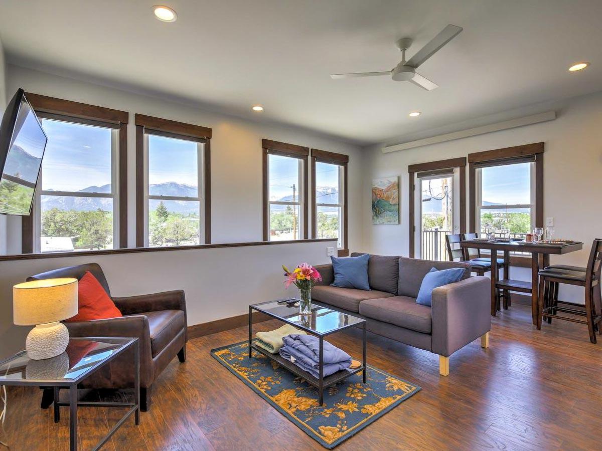 Living room interior with sofa, armchair, coffee table, dining table, and large windows showcasing mountain views.