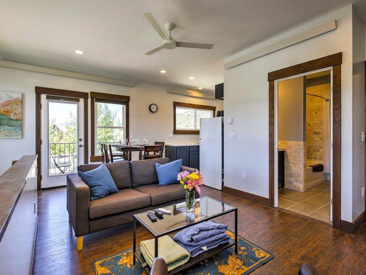 Open living area with brown sofa, glass coffee table, dining area, kitchen, and view of bathroom.