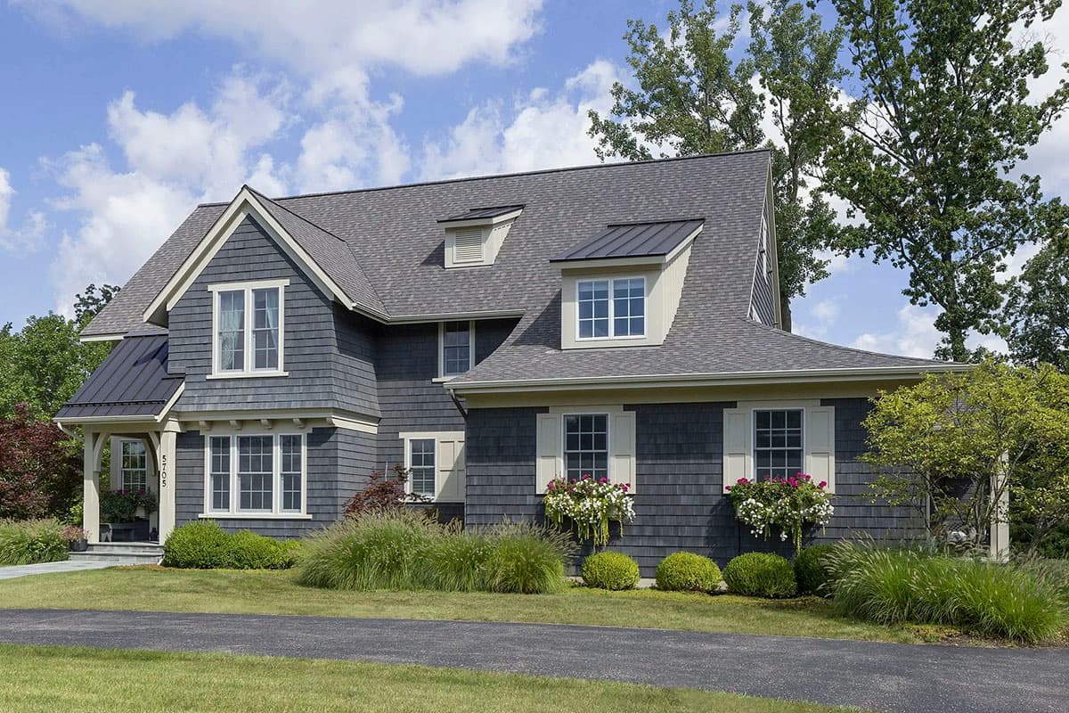 House plan exterior: Two-story home with shingle siding, gables, dormers, metal roof accents, and a covered porch.