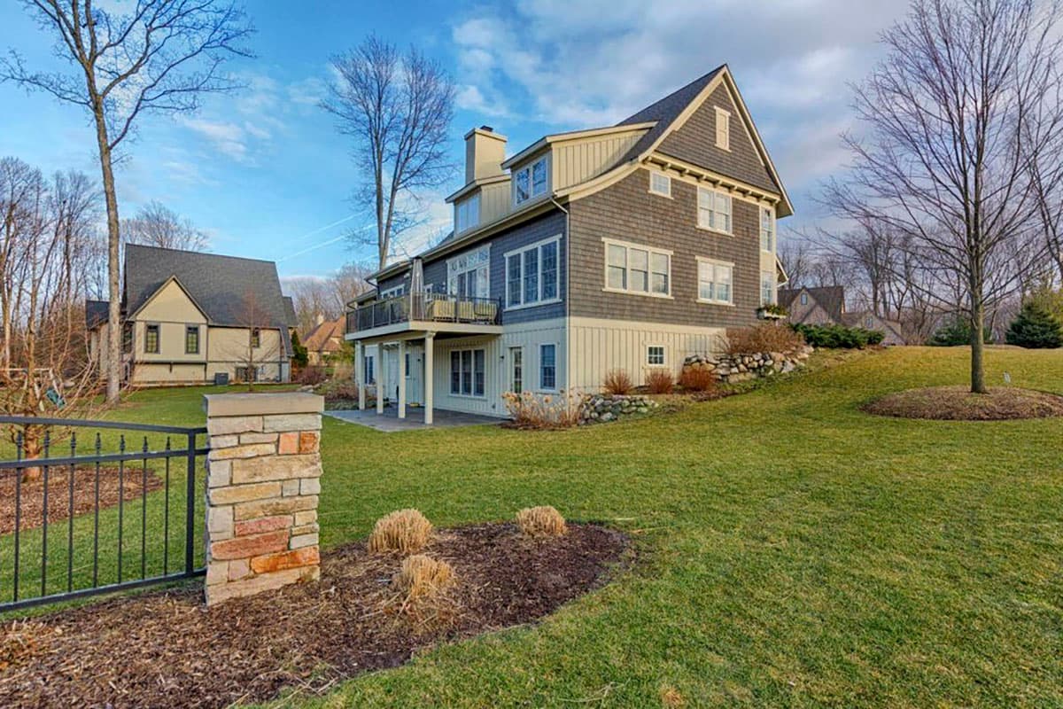 House plan exterior with multiple gables, dormers, a wraparound deck, and a stone foundation.