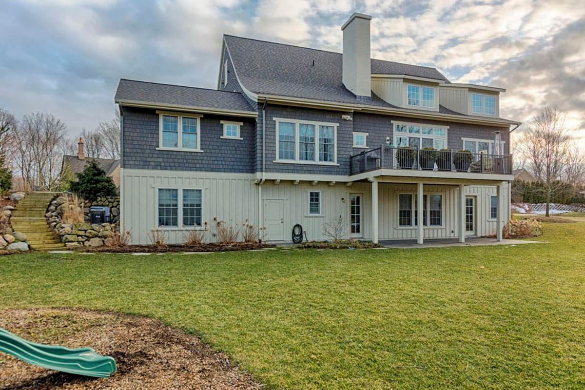 House plan exterior with a multi-story design, shingle and board siding, prominent chimney, and upper-level balcony.