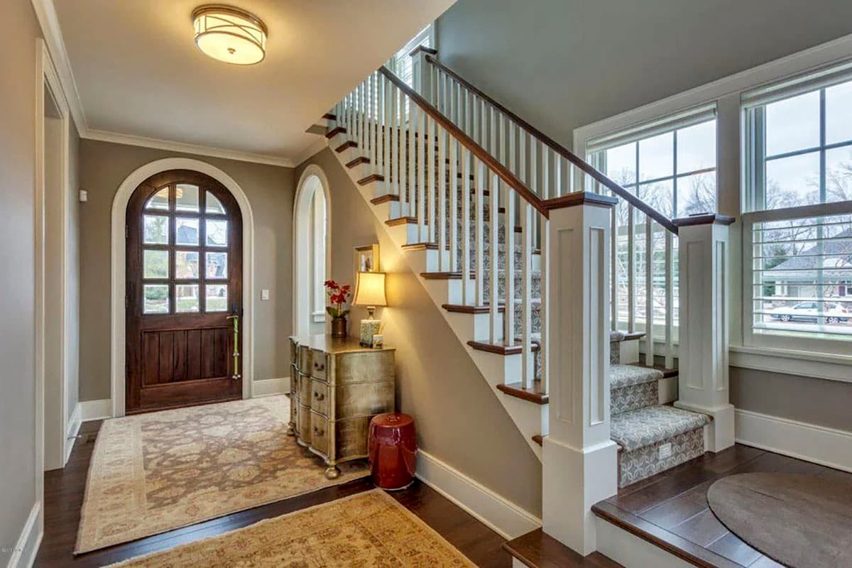 Foyer with arched wooden door, carpeted staircase with white balusters, and a console table.