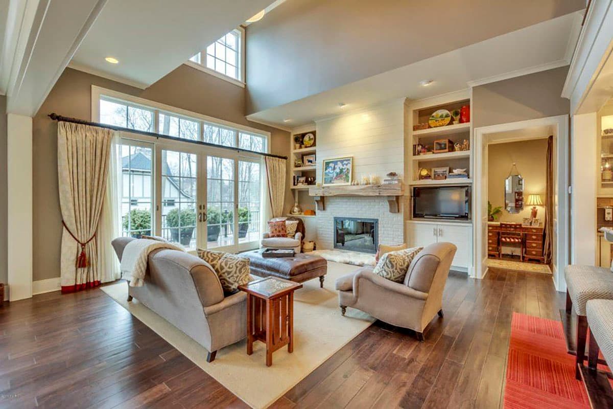 Great room with vaulted ceiling, fireplace, built-in shelving, and large windows overlooking trees.