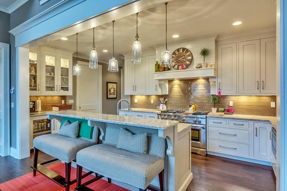 Kitchen with island seating, glass pendant lights, stainless steel range, and custom cabinetry.