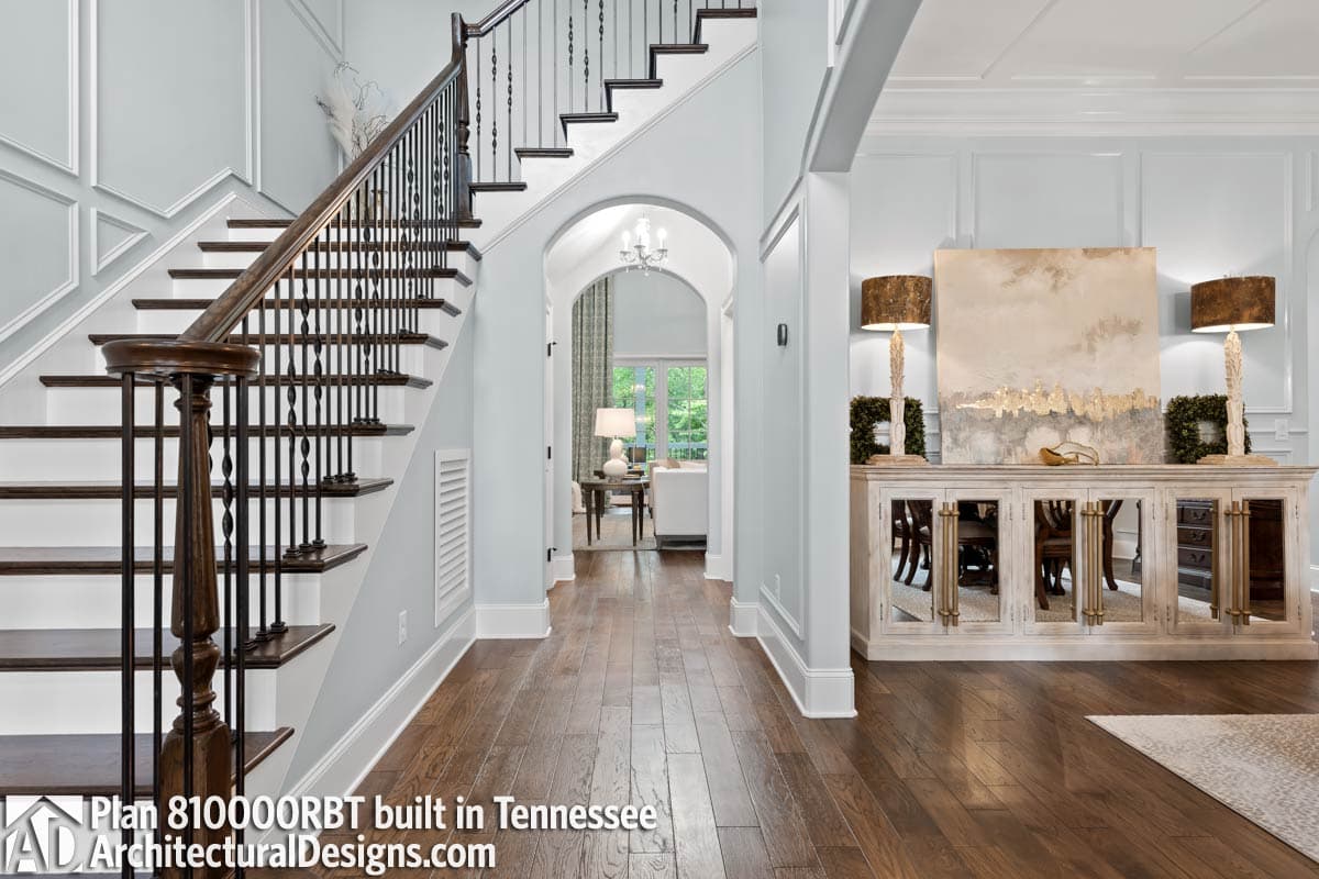 Interior view of a house plan entry with a turned staircase, wainscoting, and a mirrored sideboard.