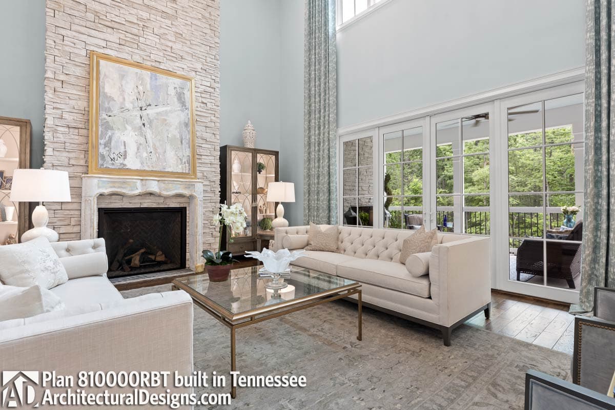 Great room with stacked stone fireplace, tufted sofa, glass coffee table, and french doors opening to balcony.