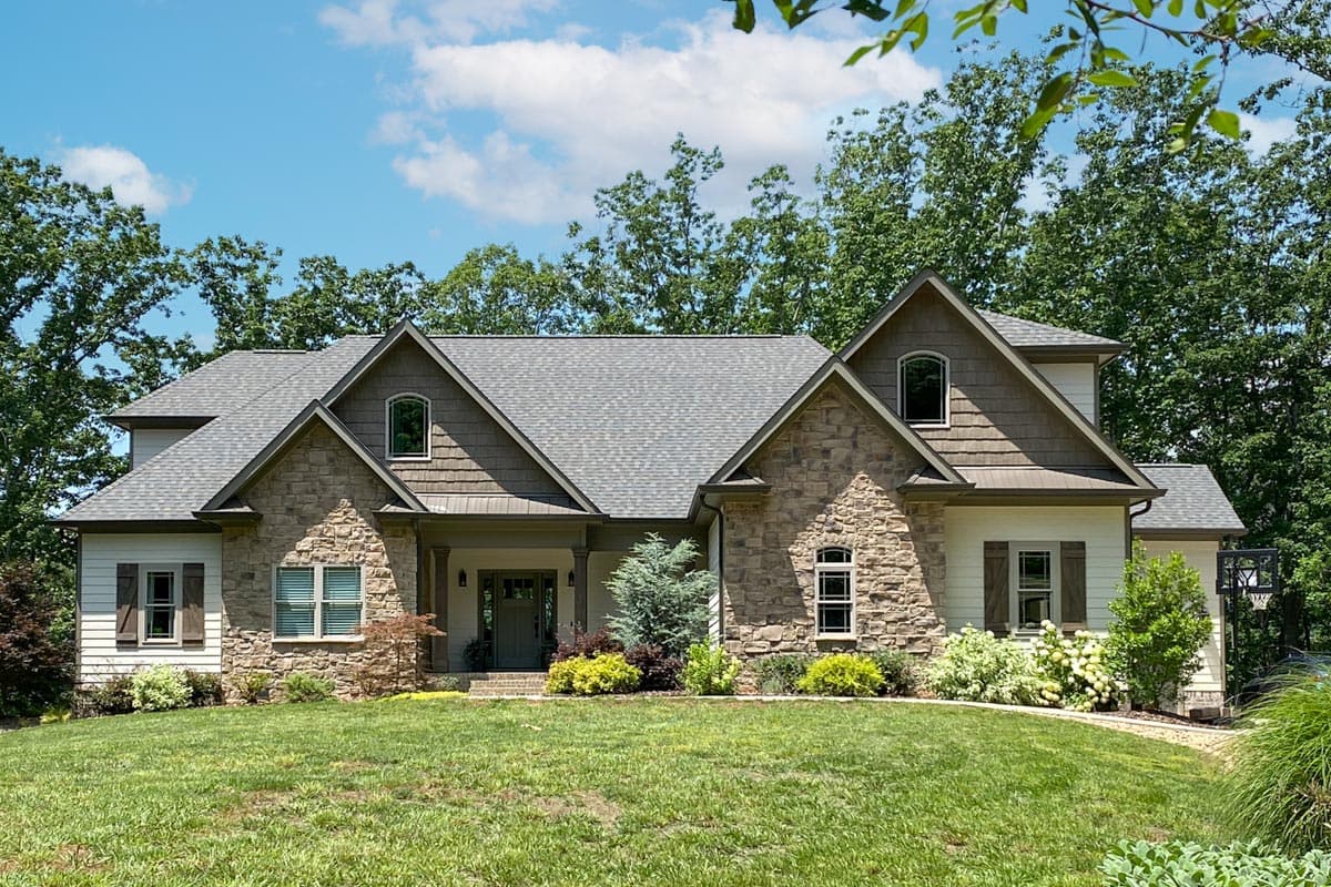 House plan exterior: Two-story home with stone accents, a covered front porch, multiple gables, and dormer windows.