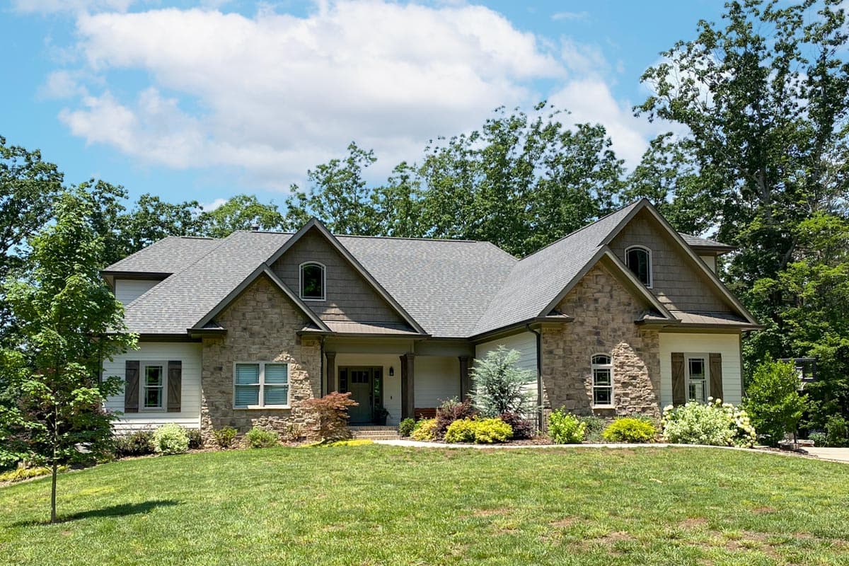 House plan exterior: two-story Modern Farmhouse with stone accents, prominent gables, dormers, and covered entry porch.