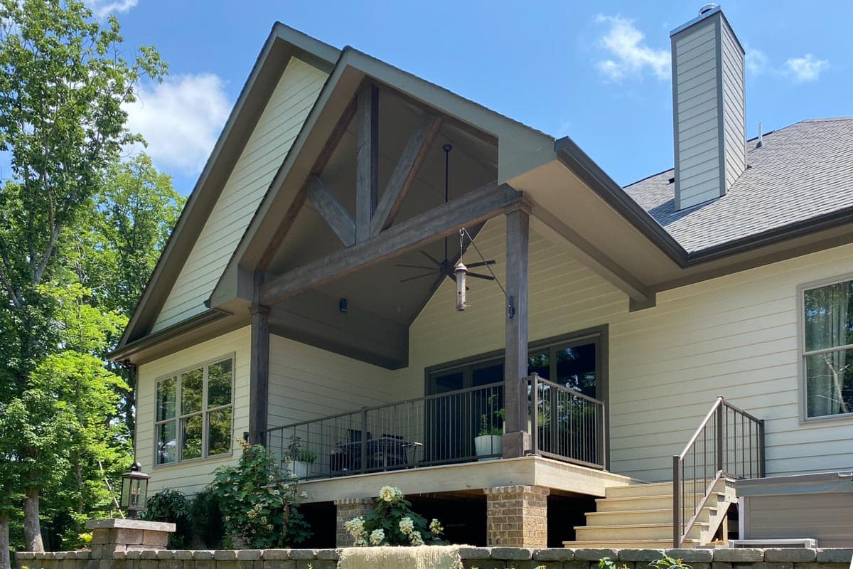 House plan exterior with gabled roof, exposed timber framing on covered porch, and stone chimney.