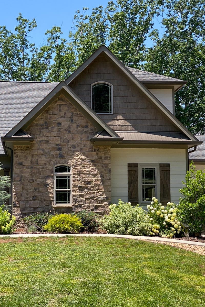 House plan exterior with stone facade, shake siding, gabled roof, arched windows, and decorative shutters.