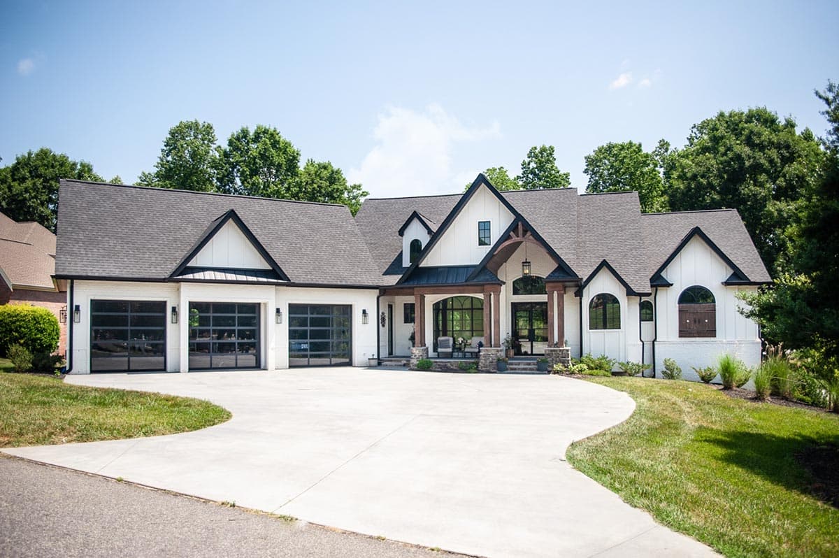 House plan exterior: Modern Farmhouse style, one-story with three glass garage doors, prominent gables, and covered entry with wood beams.