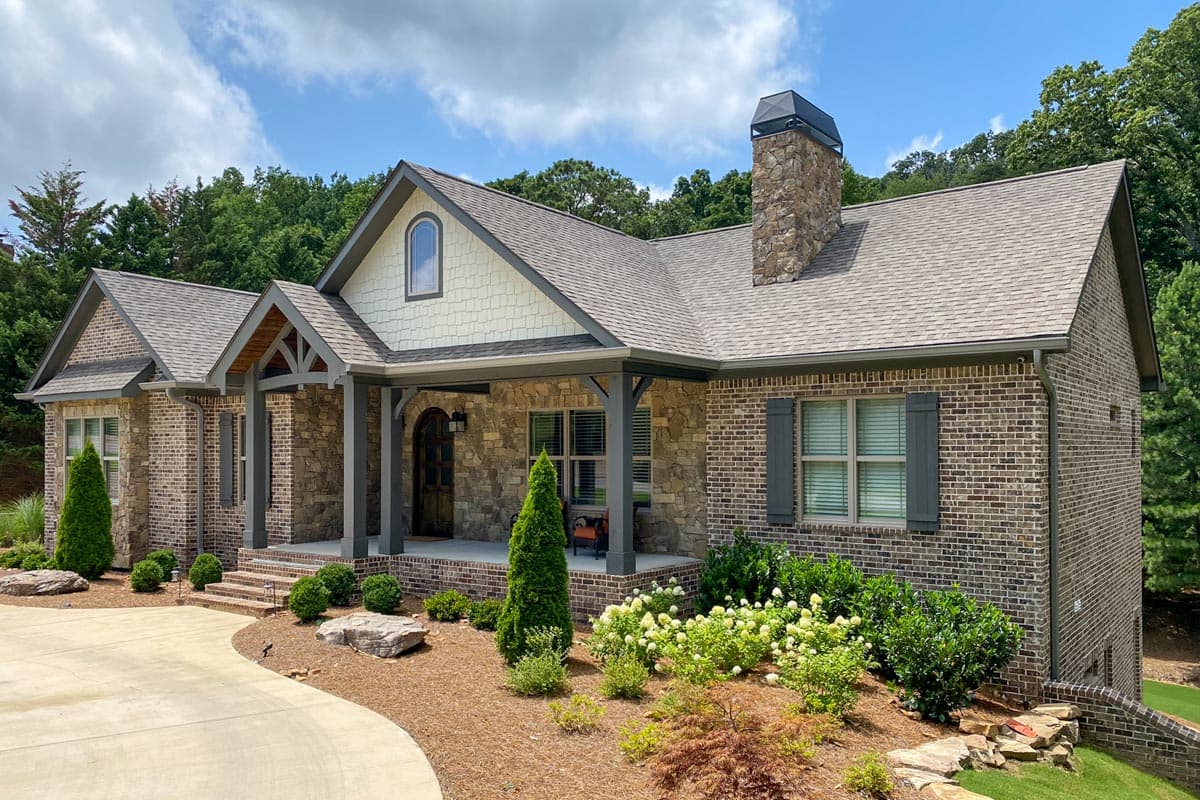 House plan exterior: Ranch-style home with stone and brick facade, covered porch with wood beams, gable dormer, and stone chimney.
