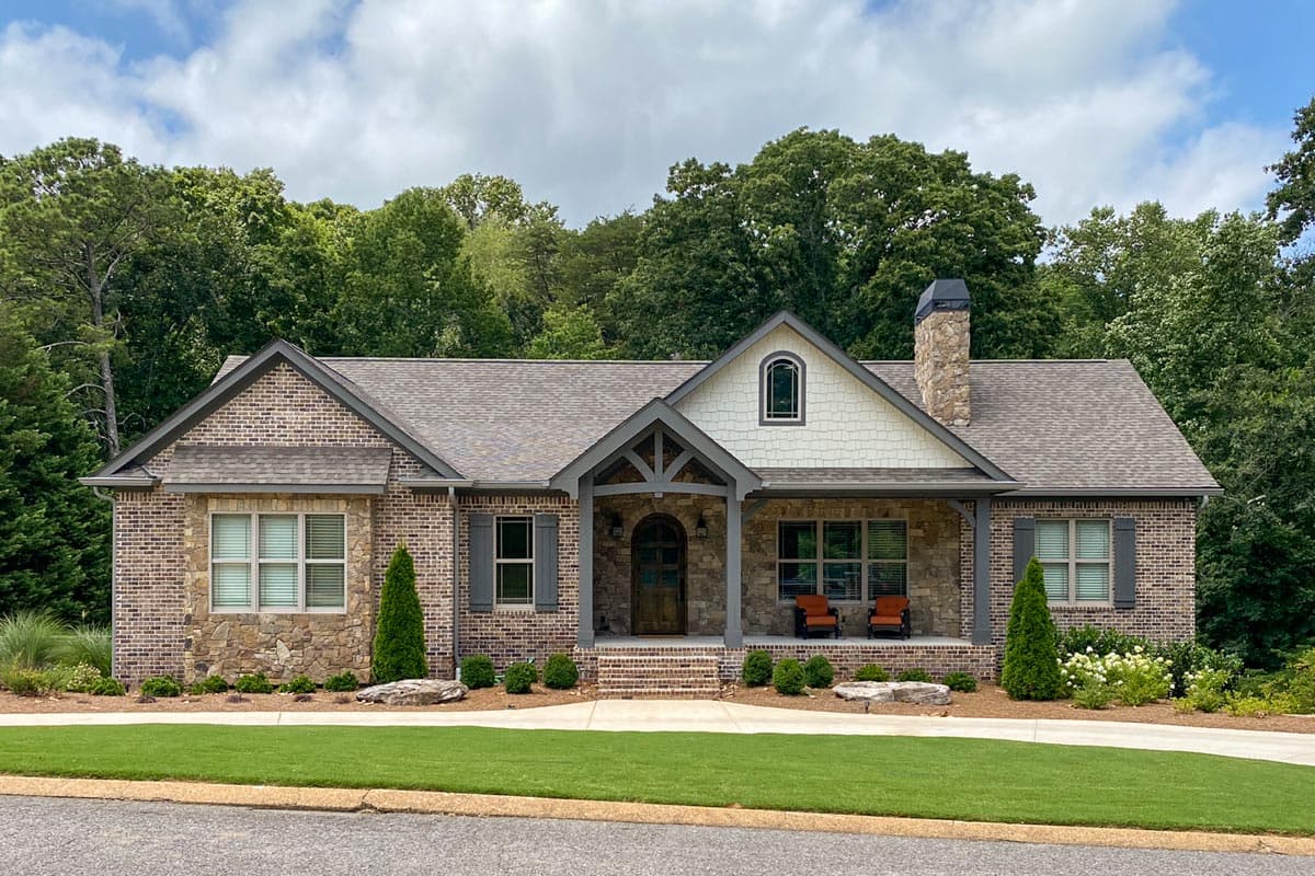 House plan exterior with brick and stone facade, covered porch, gable roof, and stone chimney. One story Craftsman style home.