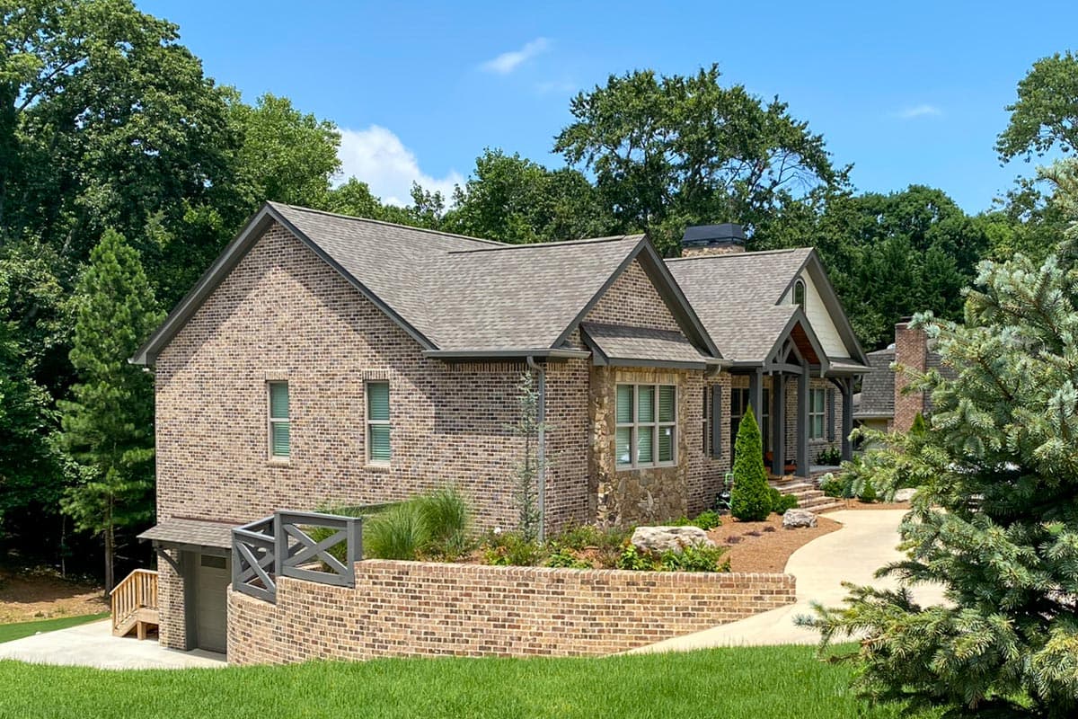 House plan exterior: Two-story brick home with stone accents, prominent gables, covered entry porch, and side-facing garage.