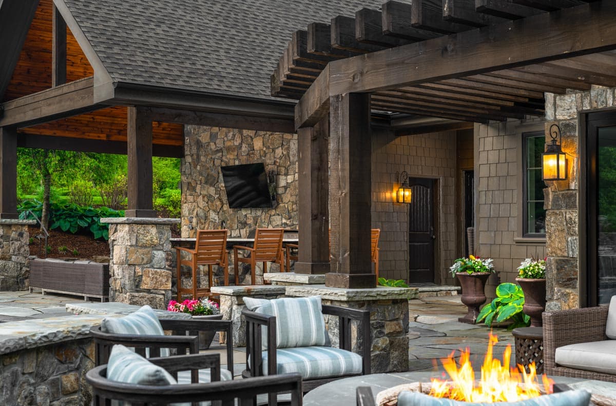 Outdoor living space with stone pillars, wood pergola, built-in bar with stools, and stone patio.