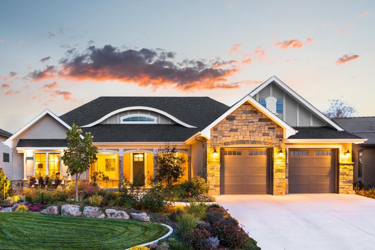 House plan exterior. Single-story home with a stone facade garage, arched roofline, and covered porch with supporting columns.