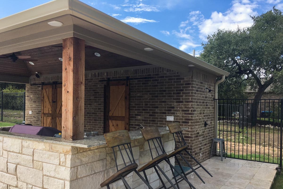 Exterior house plan with brick facade, covered patio, stone base bar, and sliding barn doors.