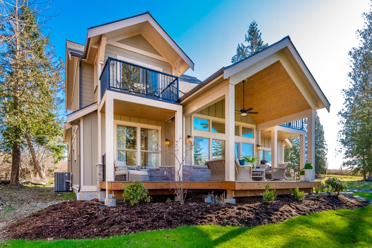 House plan exterior: two-story modern farmhouse with gabled rooflines, upper balcony, and covered patio with exposed wood ceiling.