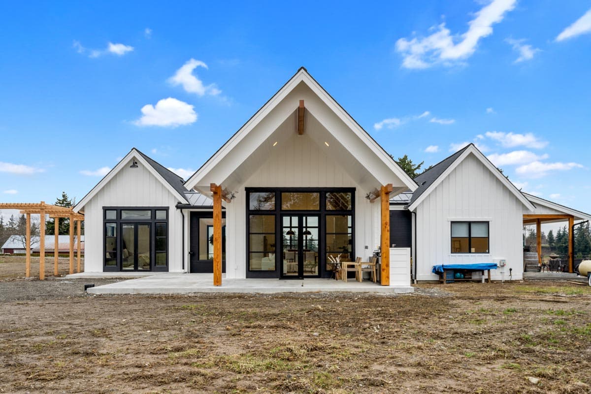 Modern Farmhouse house plan exterior with white board and batten siding, metal roof, gables, and large black-framed windows.
