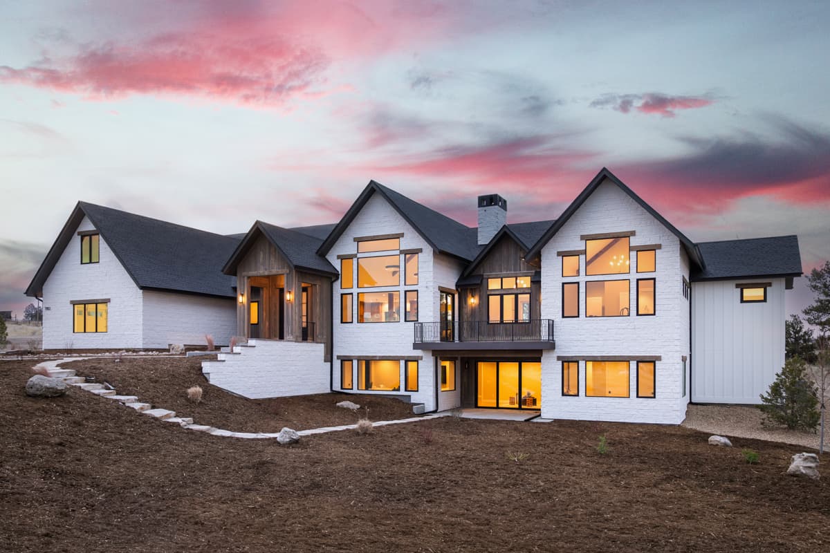 House plan exterior. Modern Farmhouse style, two-story house with gabled roof, large windows, and a combination of wood and white brick facade.