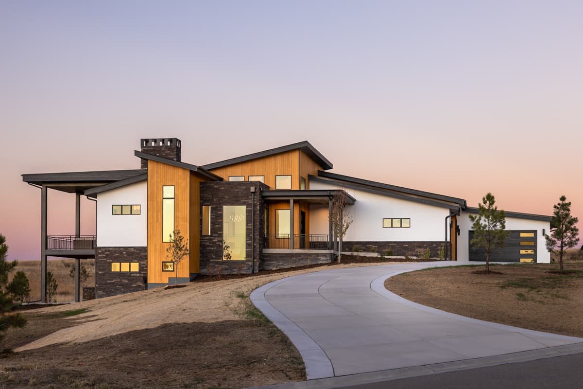 Modern house plan exterior with multiple gables, wood and stone accents, cantilevered balcony, and attached garage.