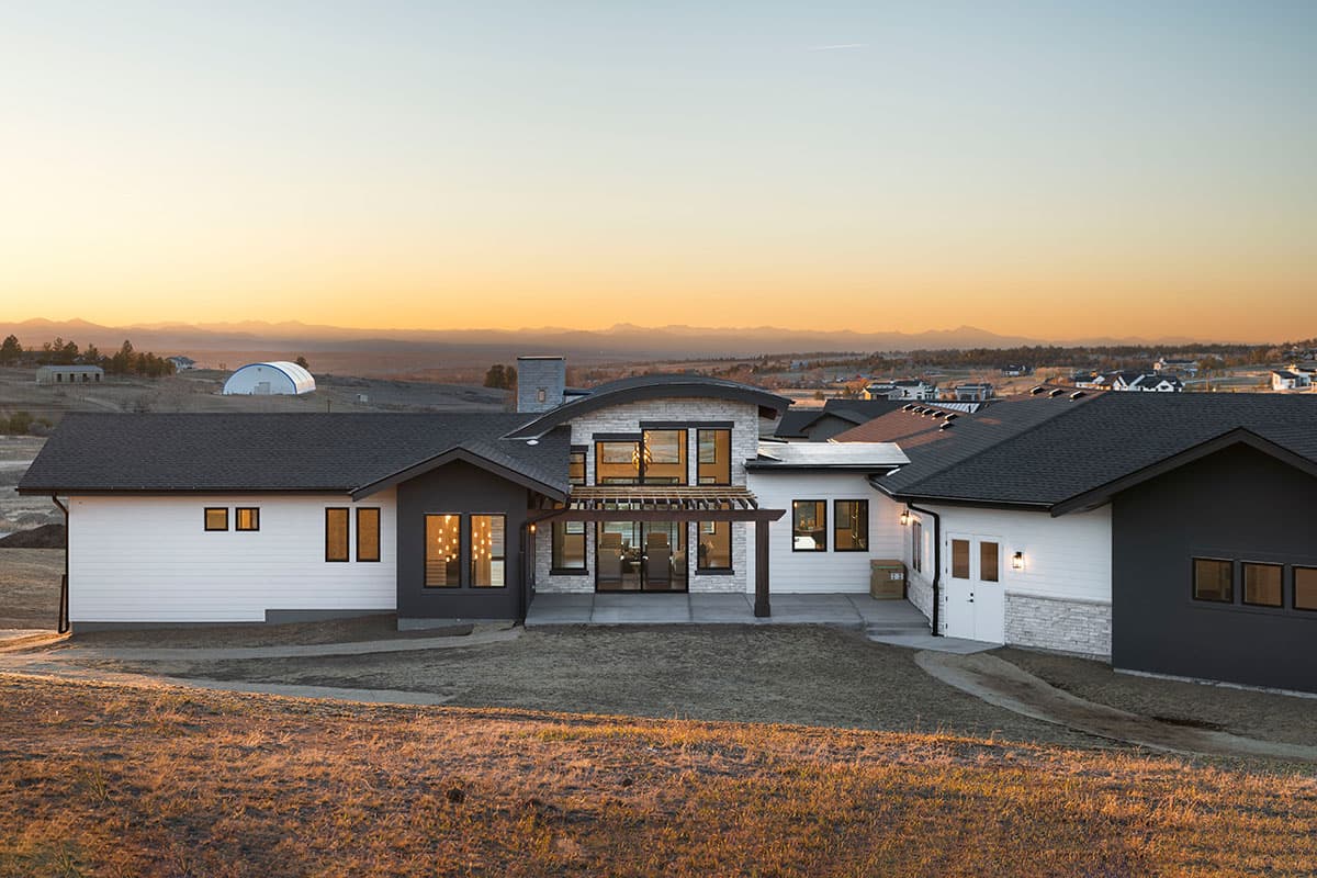 House plan exterior featuring a modern design with a curved roofline, stone accents, expansive windows, and a pergola.