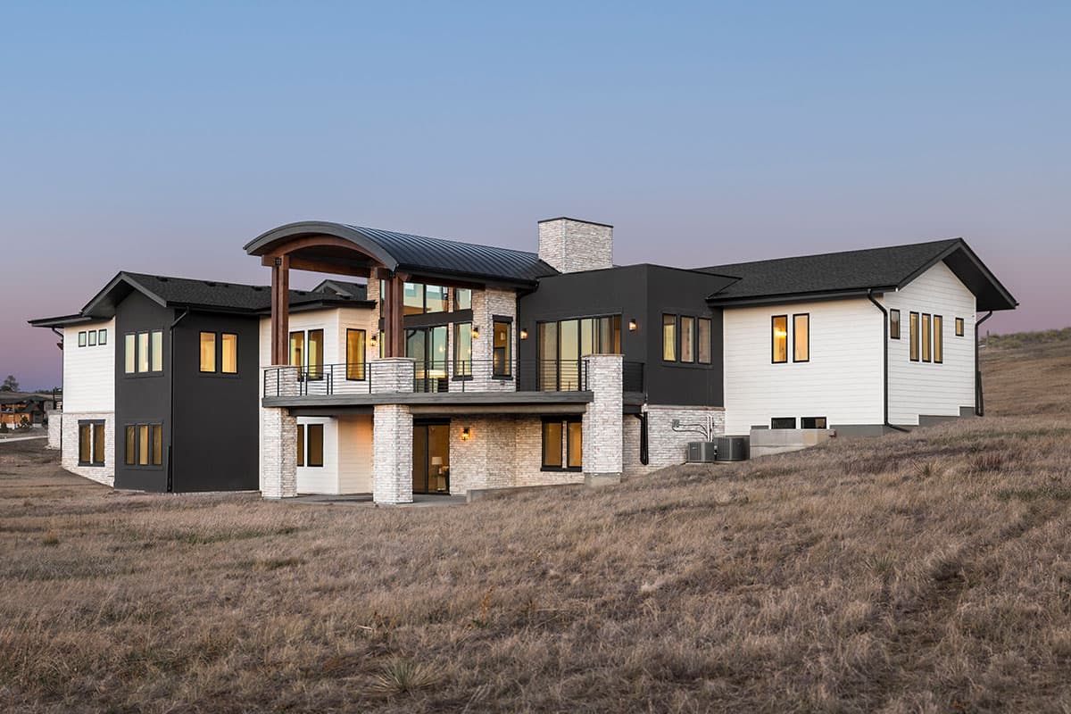 Modern house plan exterior with contrasting white siding and black stucco, stone accents, large windows, and a curved roof.