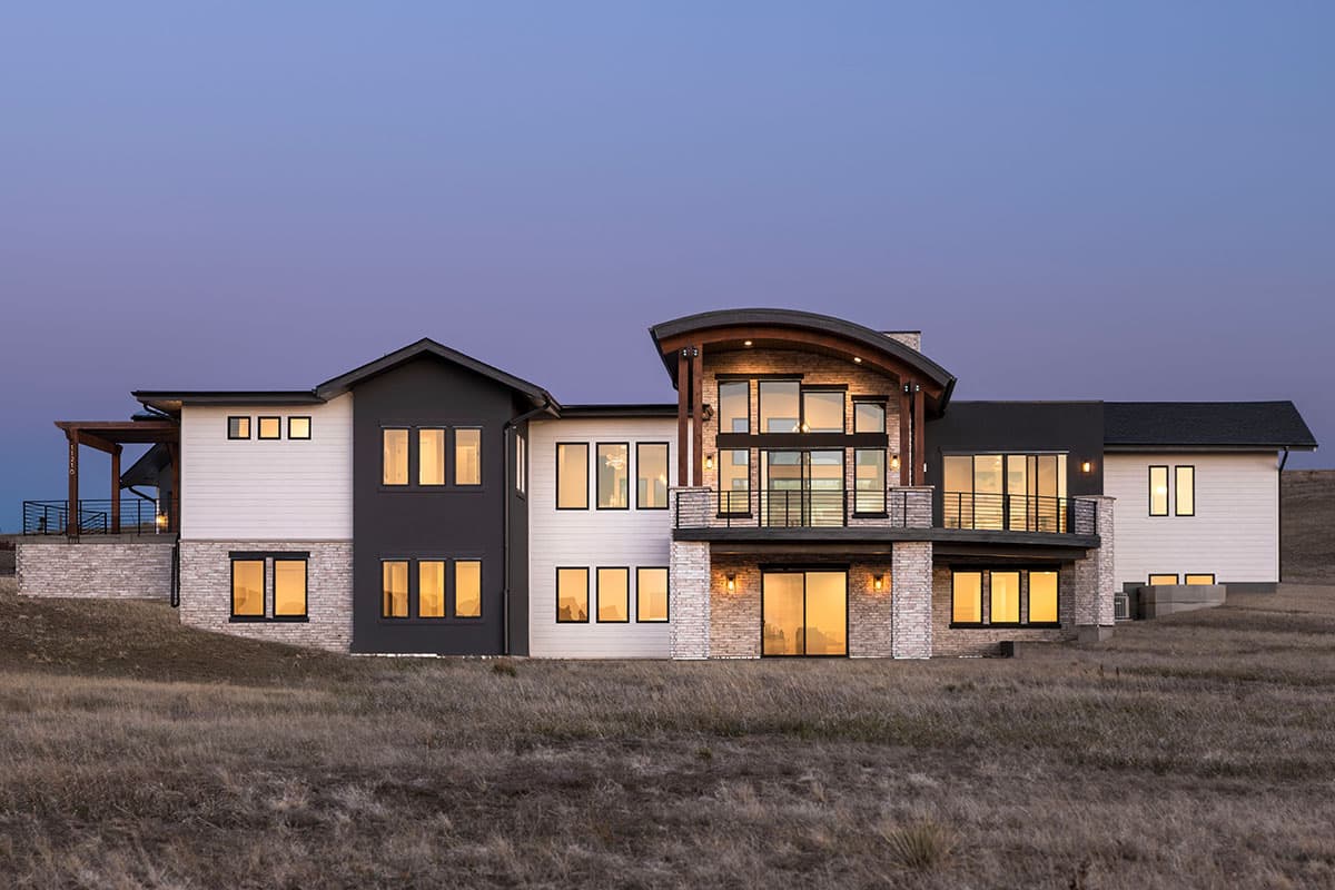 Modern house plan exterior with multiple stories, stone and white siding, dark gables, and a curved roofline over a multi-story window.