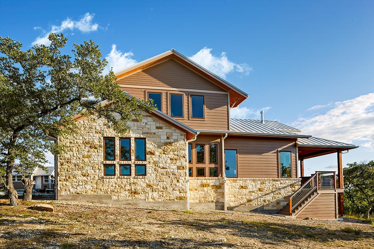 House plan exterior with stone and wood siding, metal roof, gabled rooflines, and covered deck with stairs.