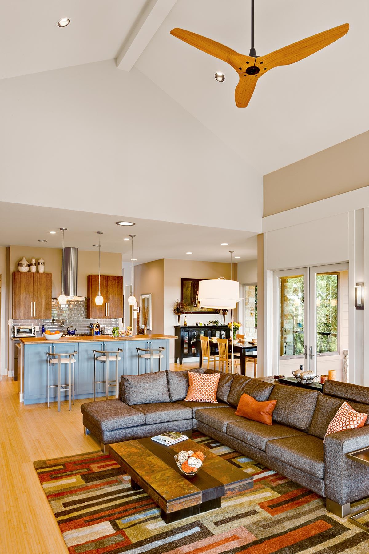 Open concept living area with a sectional sofa, island kitchen, dining area, and vaulted ceiling with fan.